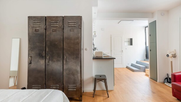 Ein Schlafzimmer mit großem Kleiderschrank, einem kleinen Hocker und einer Treppe zu einem anderen Raum.