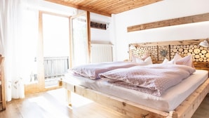 A wooden bed with patterned bedding in a room with a sloped ceiling and a view of a balcony. - Spacious House In Fugen With Terrace (Fuegen)