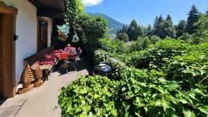 An outdoor seating area with a table and chairs, surrounded by lush greenery and a mountain view. - Spacious House In Fugen With Terrace (Fuegen)