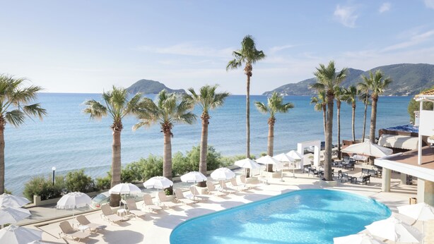 A pool area with lounge chairs and umbrellas, overlooking a body of water and hills. - Cameo Beach Resort (Zakynthos)