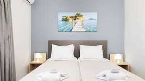 A hotel room with a bed, two bedside tables with lamps, a painting of a coastal scene, and a grey curtain. - Cameo Beach Resort (Zakynthos)