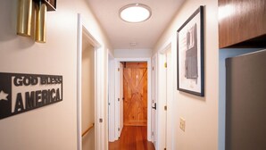 Un pasillo con una puerta de madera al final, un cartel en la pared y un cuadro enmarcado.