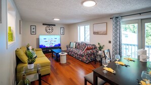 Una sala de estar con sofá, televisión, mesa de comedor con sillas y un balcón con vistas.