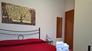 A neatly made bed with a red bedspread, a small bedside table with a bottle and a glass, and a painting on the wall. - The House OF THE SUN Brindisi (Brindisi)