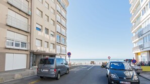 Eine Straße mit parkenden Autos, ein Gebäude mit Balkonen und einem klaren Himmel.