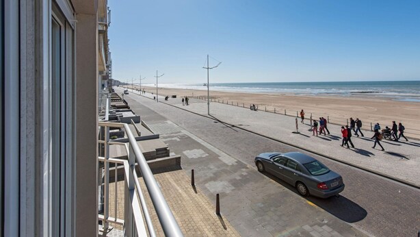 Eine Küstenpromenade mit befestigtem Gehweg, einem parkenden Auto und freiem Blick auf Strand und Meer.
