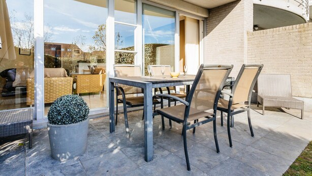 An outdoor patio with a table and chairs, a potted plant, and a view of the interior through glass doors. - Amandari Igv01 Near the Center in Koksijde (Koksijde)