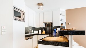 A modern kitchen with white cabinets, a black countertop, a microwave, a coffee machine, and a wooden cutting board. - Amandari Igv01 Near the Center in Koksijde (Koksijde)