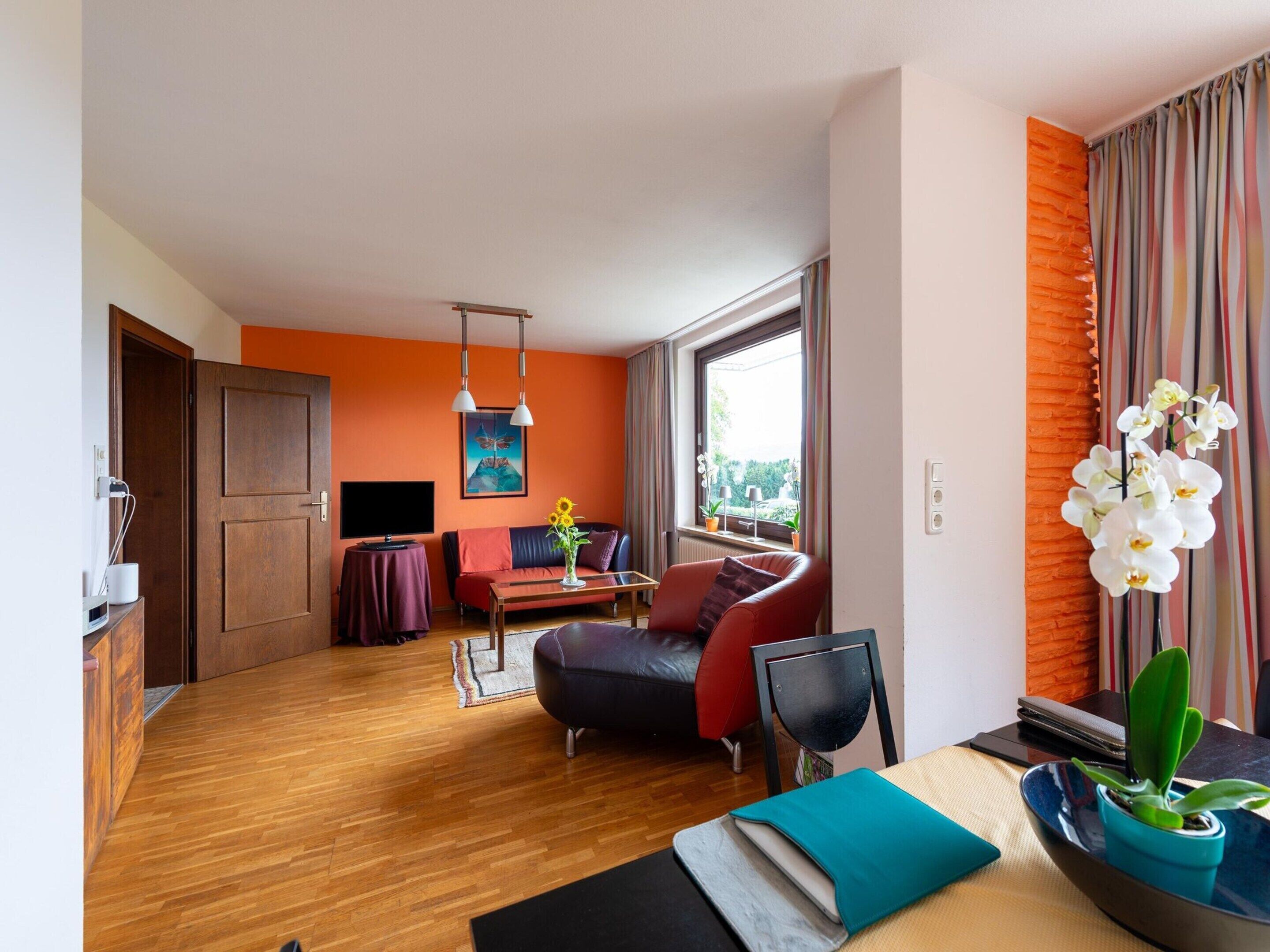 A modern hotel room with a wooden floor, a sofa, a coffee table, a TV, and a window with curtains.