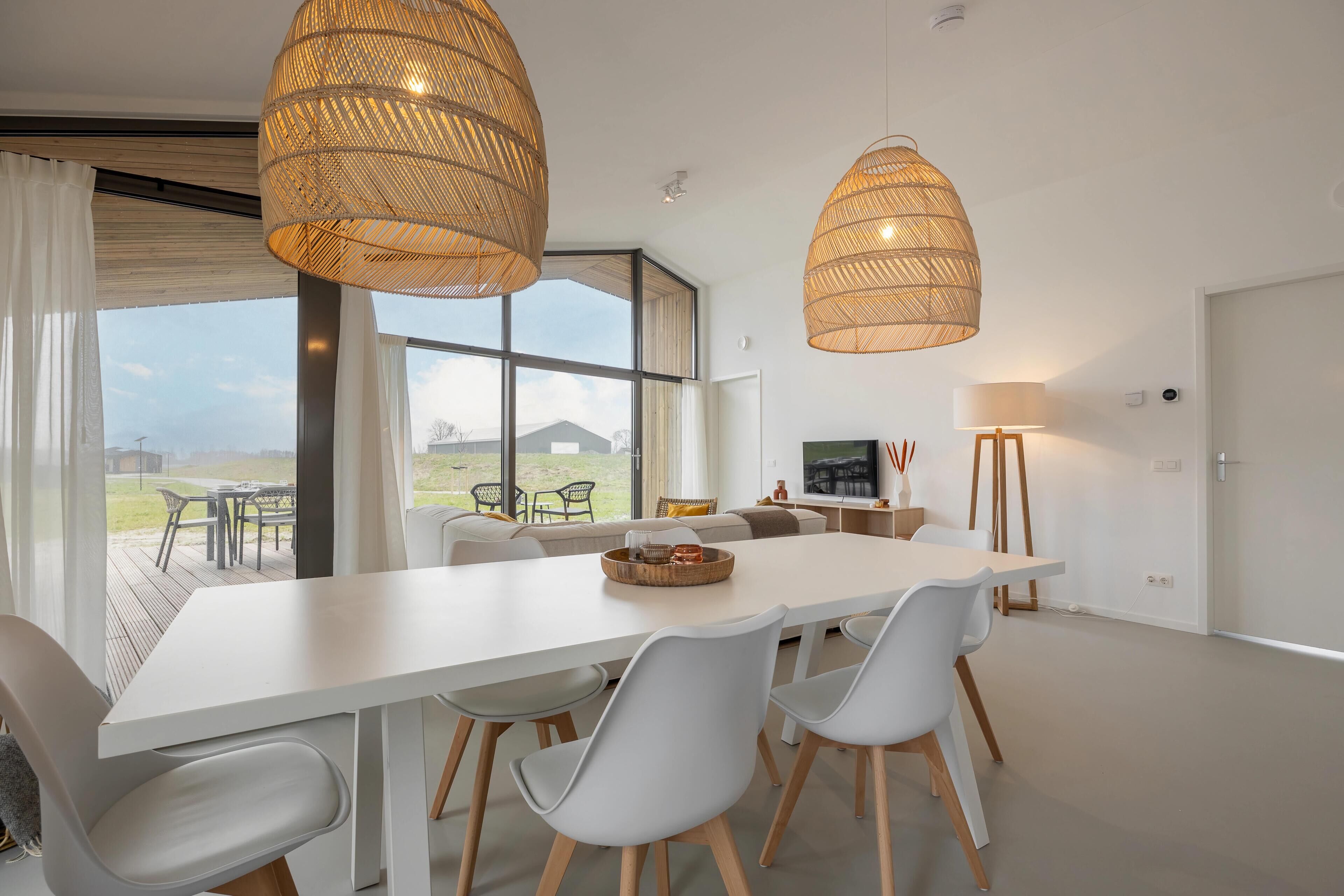 Un comedor moderno con una mesa blanca, sillas grises y lámparas colgantes de mimbre.