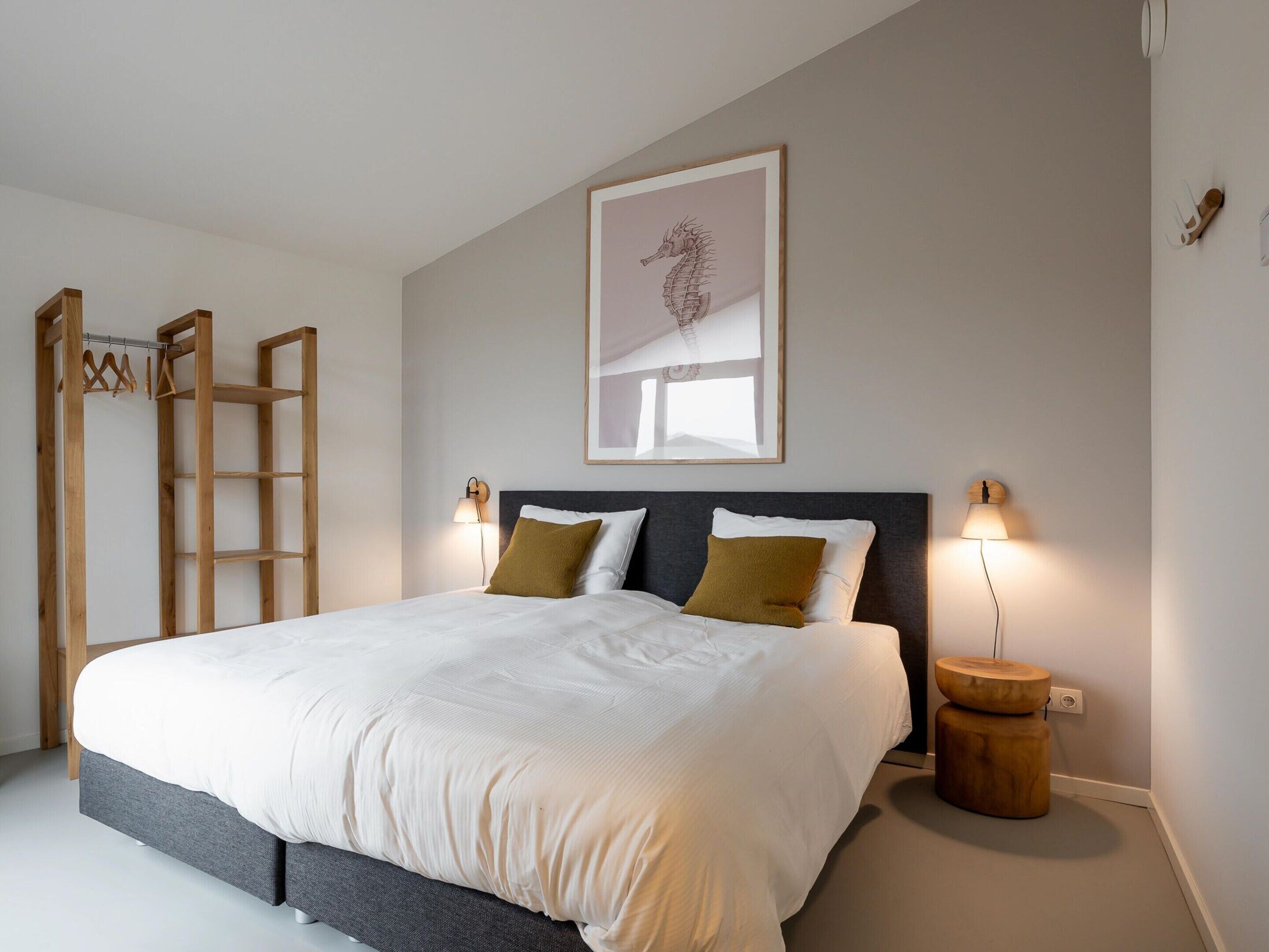 A neatly made bed with a grey headboard, two bedside lamps, and a framed seahorse artwork on the wall.