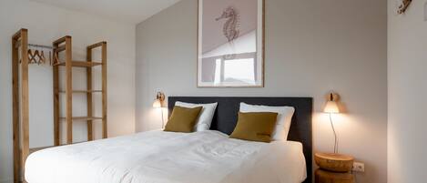 A neatly made bed with a grey headboard, two bedside lamps, and a framed seahorse artwork on the wall.
