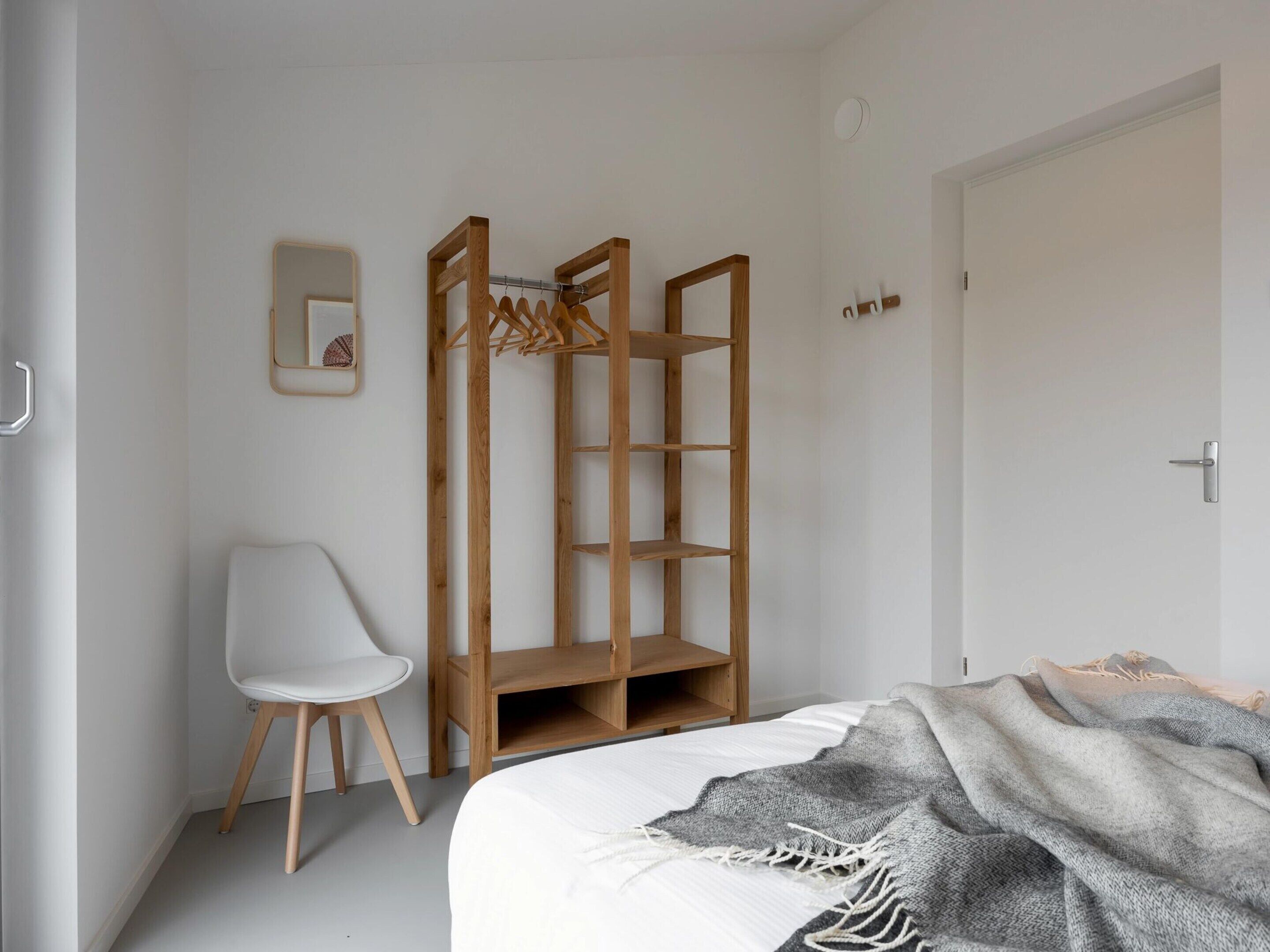 A bedroom with a bed, a wooden wardrobe, a white chair, and a door.