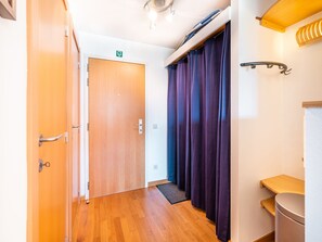 A hallway with wooden flooring, a closed door, purple curtains, a small wooden shelf, and a light fixture on the ceiling. - Cosy Apartment in Koksijde Near the Beach (Koksijde)
