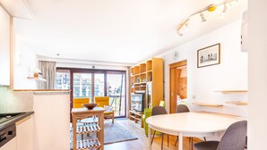 A modern, well-lit room with a wooden dining table, chairs, and a kitchen area with a stove. - Cosy Apartment in Koksijde Near the Beach (Koksijde)