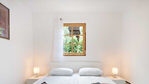 A double room with two beds, a window with a view of greenery, and bedside lamps.