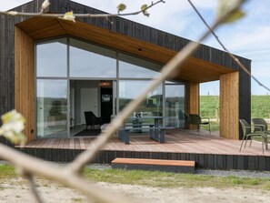 A modern house with large glass windows, a wooden deck, and outdoor seating. - Lovely Holiday Home in the Nature (Wissenkerke)