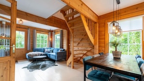 A wooden interior with a staircase, a blue sofa, a dining table with chairs, and large windows. - Holiday Home by Zuidlaardermeer With Jetty (Kropswolde)