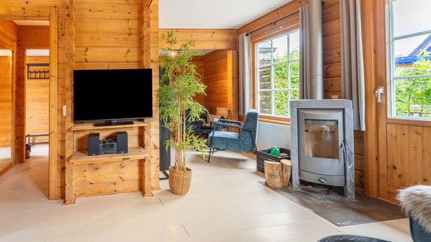 A wooden cabin interior with a TV, a fireplace, a dining area, and a large window. - Holiday Home by Zuidlaardermeer With Jetty (Kropswolde)