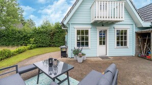 A light blue house with a balcony, a patio with a table and chairs, and a well-maintained garden. - Holiday Home by Zuidlaardermeer With Jetty (Kropswolde)
