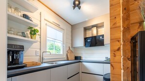 A modern kitchen with white cabinets, a black countertop, a coffee machine, and a window with a view of greenery. - Holiday Home by Zuidlaardermeer With Jetty (Kropswolde)