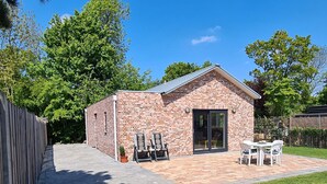 A small brick building with a tiled patio, a glass door, and a seating area with chairs and tables.