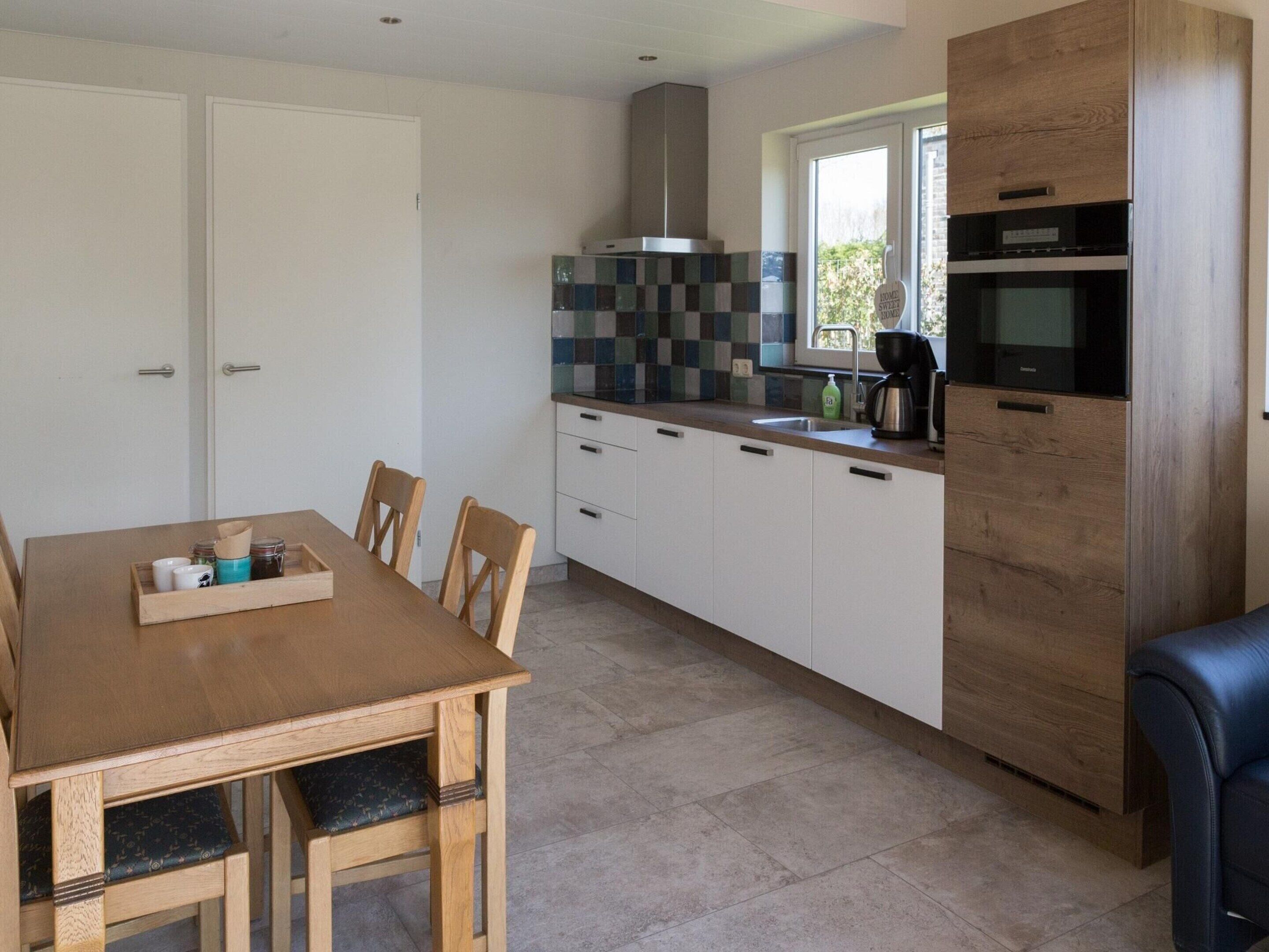 A modern kitchen with white cabinets, a wooden dining table, and a built-in oven.