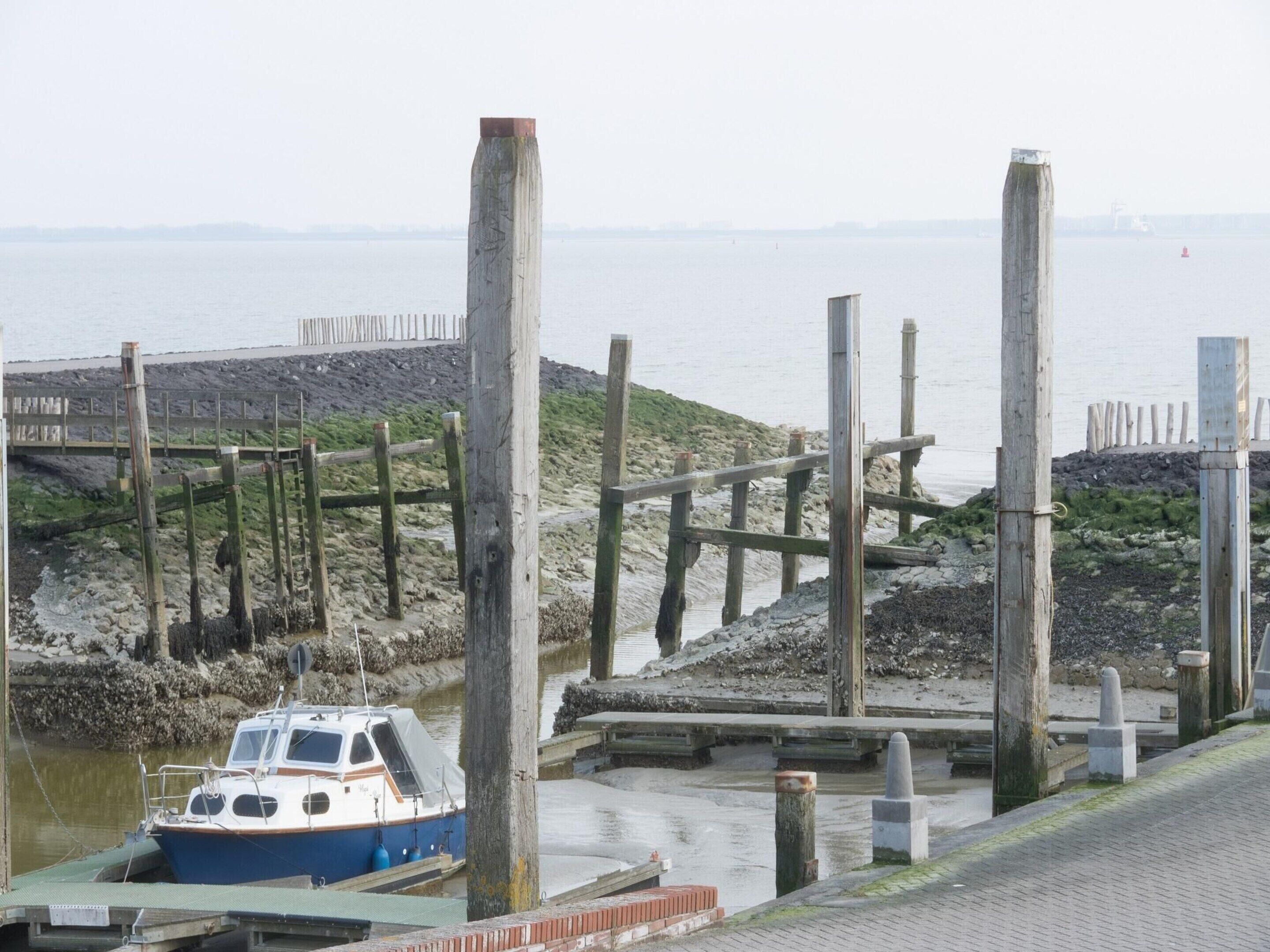 A boat docked at a pier with a rocky shoreline and a distant view of the sea.