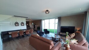 Un soggiorno moderno con divano, tavolino e televisore. C'è un'area pranzo con sedie e tavolo. La stanza ha ampie finestre e un camino.