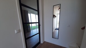 Un corridoio con una porta scorrevole in vetro che dà su un balcone, un grande specchio a parete e un interruttore della luce.