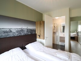 Habitación de hotel con cama, cabecera de madera, un cuadro grande en la pared, zona de ducha y baño con espejo.
