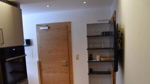 Una cocina con puerta de madera, horno empotrado y un estante con utensilios de cocina.
