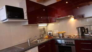 Una cocina moderna con armarios rojo oscuro, un lavamanos de acero inoxidable, un microondas, una estufa y varios utensilios de cocina.