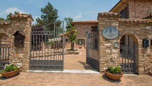 Una villa de piedra con entrada porticada, un cartel que indica 'Villa' y un camino de ladrillo que conduce al edificio principal.