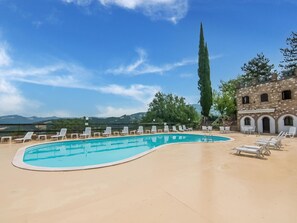 Una piscina con sillones de descanso, un edificio de piedra con arcos y vistas a colinas distantes.