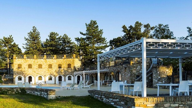 Un patio con piscina, mobiliario exterior y un edificio de piedra con arcos.