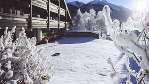 A wooden building with a sloped roof and multiple balconies, surrounded by snow-covered trees and mountains in the background. - Dachgeschoss-atelier (Seefeld in Tirol)
