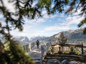 A wooden pedestrian bridge with metal railings, leading to a mountain view.
