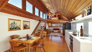 A spacious dining area with wooden furniture, a staircase leading to an upper level, and a kitchen with modern appliances. - Dachgeschoss-atelier (Seefeld in Tirol)