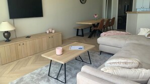 Un salon moderne comprenant un canapé, une table basse, un téléviseur et un coin repas avec des chaises et une table.