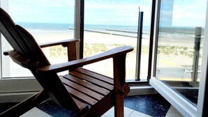 Ein Holzstuhl neben einem großen Fenster mit Blick auf Strand und Meer.