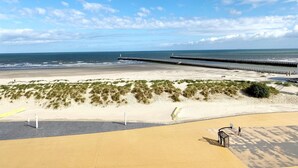 Ein Strand mit einer langen Seebrücke, die sich ins Meer erstreckt, einem Sandbereich mit Dünen und einem Basketballplatz im Vordergrund.