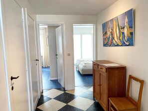A hallway with a checkered floor, a wooden cabinet, and a painting of sailboats on the wall. - Seaview Apartment in Nieuwpoort (Nieuwpoort)