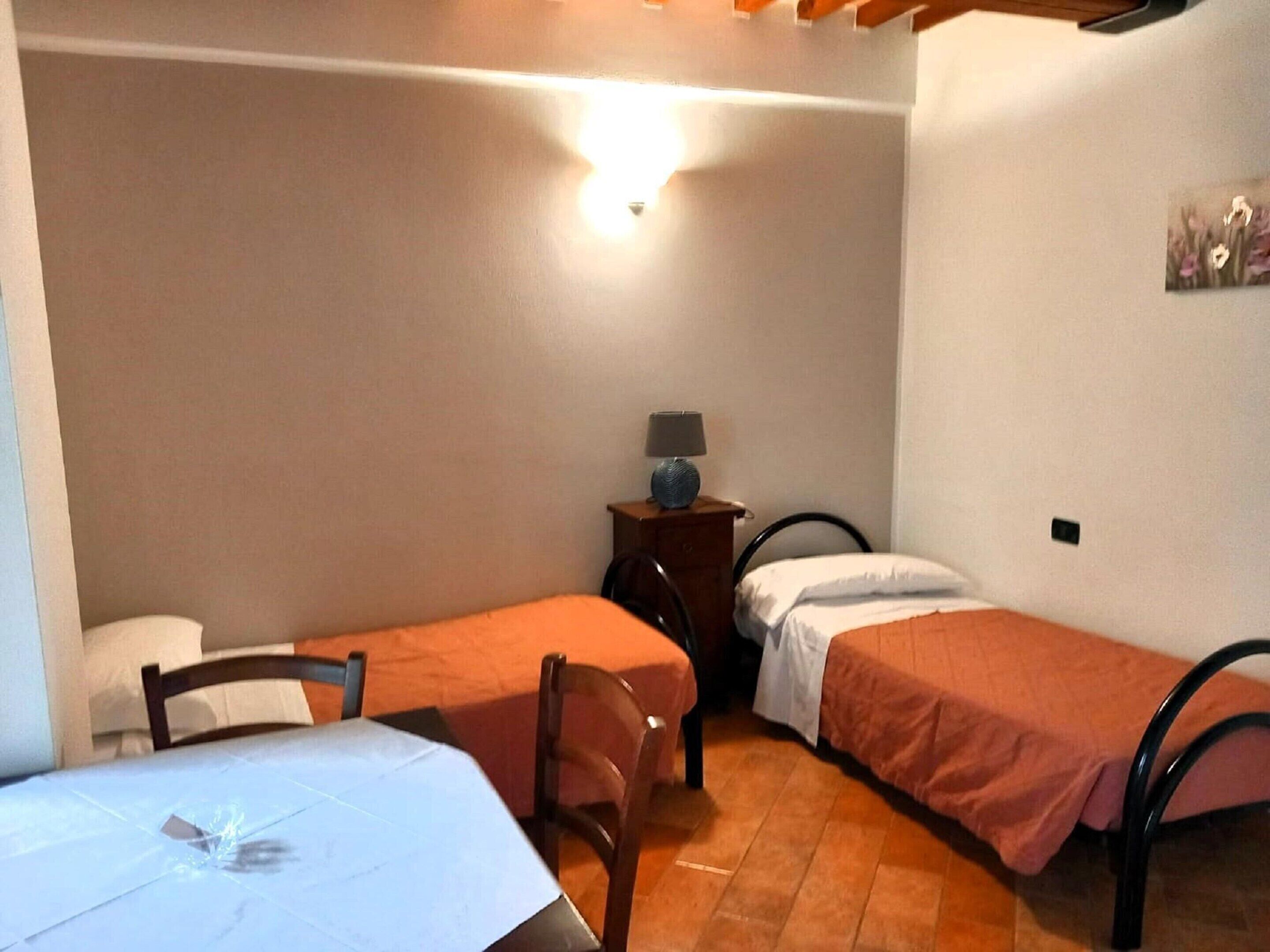 Een kleine, compacte kamer met twee eenpersoonsbedden, een tafel en een stoel.