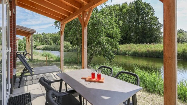 Une terrasse extérieure avec une table et des chaises, une pergola en bois et une vue sur une rivière et des arbres.