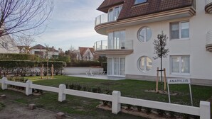 A two-story residential building with a white exterior, a balcony on the upper floor, and a small garden area with a white fence. - Apartment in Nieuwpoort With Sea Views (Nieuwpoort)