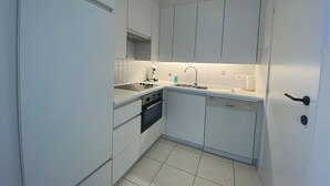 A compact kitchen with white cabinets, a built-in oven, a sink, and a dishwasher. - Apartment in Nieuwpoort With Sea Views (Nieuwpoort)