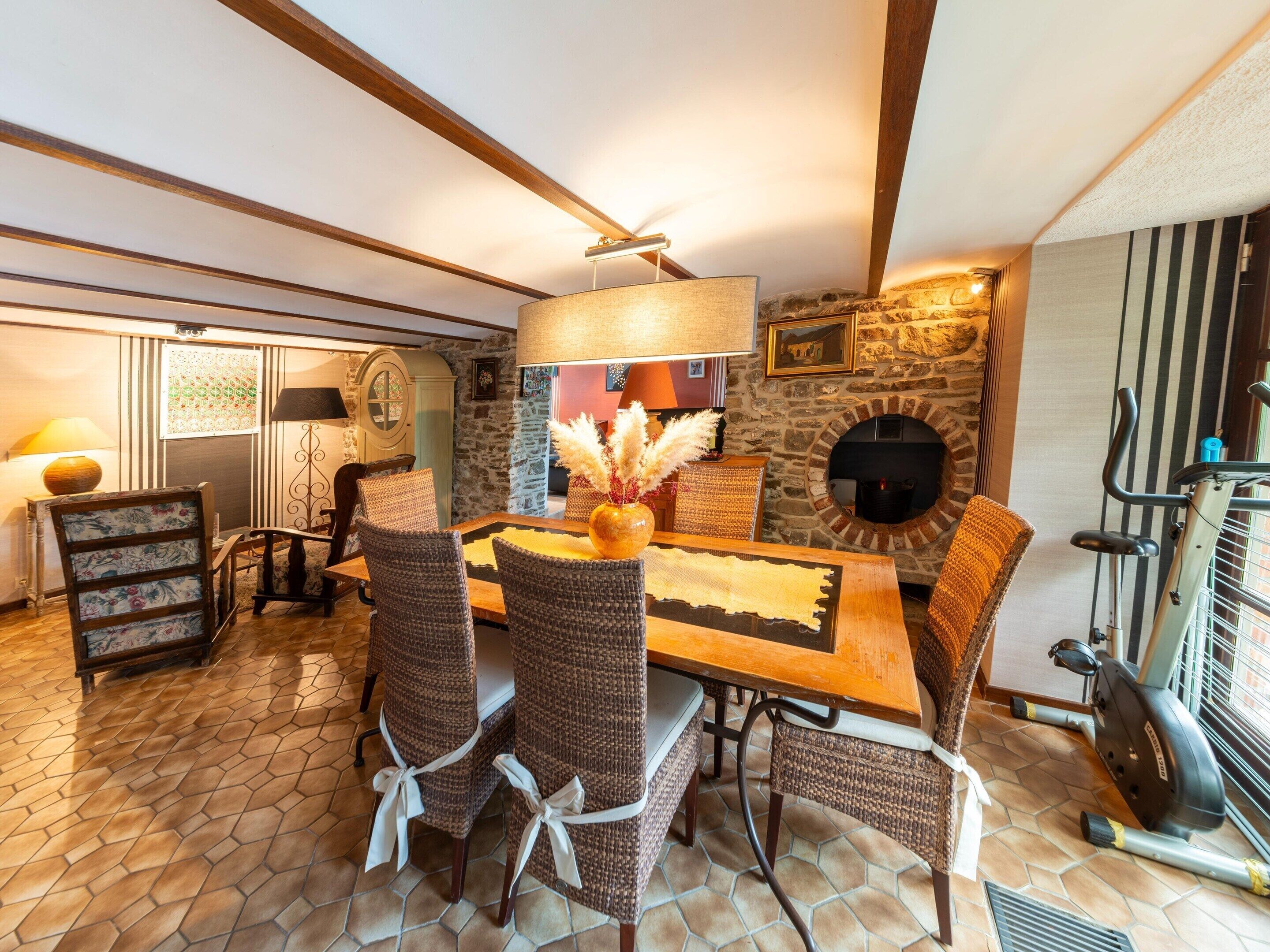 A dining area with a wooden table and wicker chairs, a stone wall, and a fireplace.
