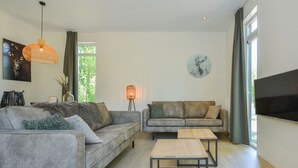 Un salon moderne avec deux canapés, une table basse, un lampadaire et un téléviseur fixé au mur.