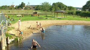 Een zandstrand met een houten constructie, een kleine vijver en fietsen op de achtergrond.
